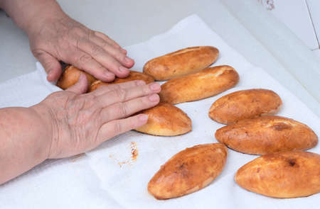 Senior woman hands with ready-made pies with apple filling just from the oven. Selective focus. Process of making pies with apple filling. Cooking at home concept. Tradition home-made foodの写真素材