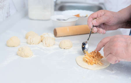Senior woman hands put the apple filling on the dough for pies on a white kitchen table. Selective...
