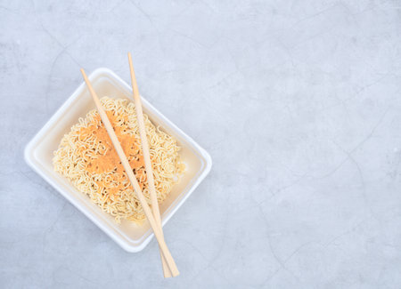Uncooked instant Chinese curly noodles in takeout packaging with wood sticks. Selective focus. Asian...