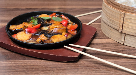 Delicious asian food in cast-iron pan on wooden background with chopsticks. Selective focus. Asian food concept.の写真素材