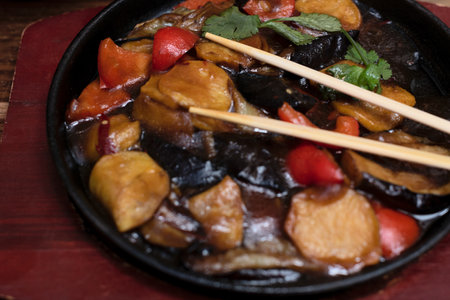 Delicious asian food in cast-iron pan on wooden background with chopsticks. Selective focus. Asian food concept.の写真素材