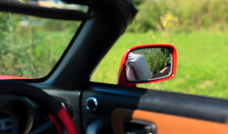 Reflection of woman in white dress near red cabriolet in car mirror close up with selective focus. Road trip enjoying freedom concept . High quality photoの写真素材