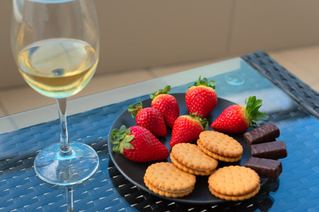 Strawberries and sweets on plate close up with selective focus with glass of champagne or white wine on a table on balcony or terrace. Luxury lifestyle, romance concept. High quality photoの写真素材