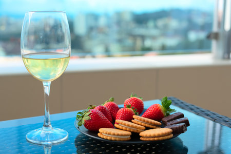 Strawberries and sweets on plate with glass of champagne or white wine on a table on balcony or terrace with blurred view on city rooftops and sea. Selective focus. Luxury lifestyle, travel concept. High quality photoの写真素材