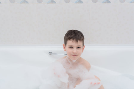Happy boy takes a bath with lush foam playing with bubbles. Personal hygiene, healthcare concept. High quality photoの写真素材