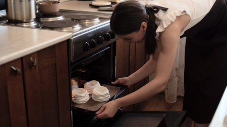 Woman pastry chef taking out baked homemade meringue cake Pavlova from oven. Selective focus. Process of cooking at home concept. High quality photoの写真素材