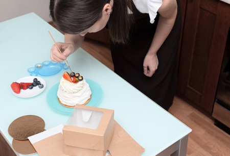 Woman pastry chef at home making finishing touches for homemade meringue cake Pavlova with summer fresh berries with selective focus. Homemade pastry, delicious sweets concept. High quality photoの写真素材