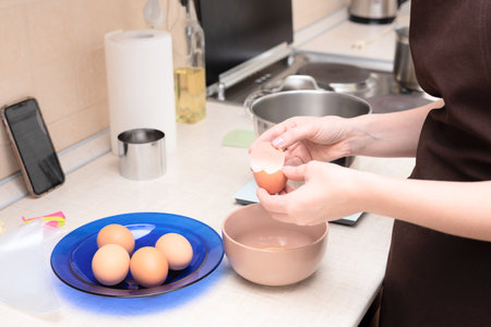 Woman adding egg whites in bowl making homemade meringue cake Pavlova by online recipe from her phone. Selective focus. Process of cooking at home concept. High quality photoの写真素材