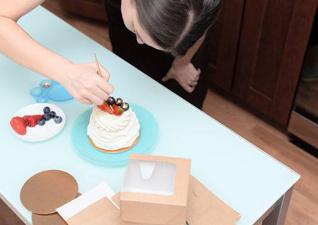 Woman pastry chef at home making finishing touches for homemade meringue cake Pavlova with summer fresh berries with selective focus. Homemade pastry, delicious sweets concept. High quality photoの写真素材