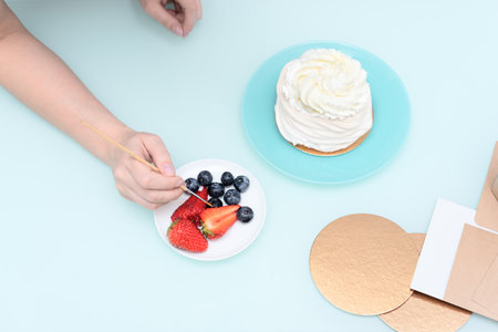 Womans hands decorating homemade meringue cake Pavlova with summer fresh berries with selective focus. Homemade pastry, delicious sweets concept. High quality photoの写真素材