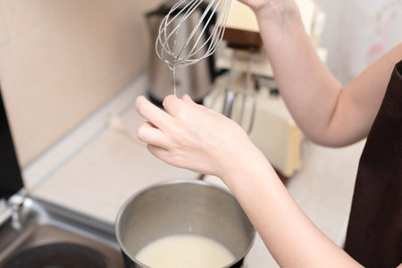 Woman whipping egg whites with manual whisk in bowl making homemade meringue cake Pavlova. Selective...