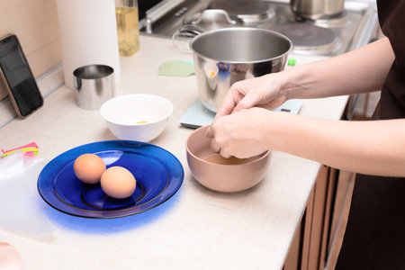 Woman adding egg whites in bowl making homemade meringue cake Pavlova by online recipe from her phone. Selective focus. Process of cooking at home concept. High quality photoの写真素材