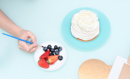 Womans hands decorating homemade meringue cake Pavlova with summer fresh berries with selective focus. Homemade pastry, delicious sweets concept. High quality photoの写真素材