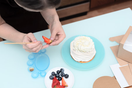 Woman pastry chef at home decorating homemade meringue cake Pavlova with summer fresh berries with selective focus. Homemade pastry, delicious sweets concept. High quality photoの写真素材