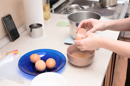Woman adding egg whites in bowl making homemade meringue cake Pavlova by online recipe from her phone. Selective focus. Process of cooking at home concept. High quality photoの写真素材
