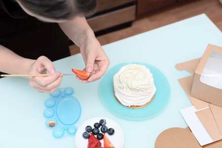 Woman pastry chef at home decorating homemade meringue cake Pavlova with summer fresh berries with selective focus. Homemade pastry, delicious sweets concept. High quality photoの写真素材