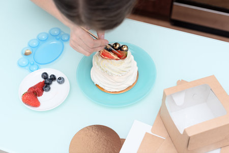 Woman pastry chef at home making finishing touches for homemade meringue cake Pavlova with summer fresh berries with selective focus. Homemade pastry, delicious sweets concept. High quality photoの写真素材