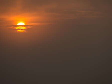 The disc of the rising sun shines through the rare clouds on a foggy morning