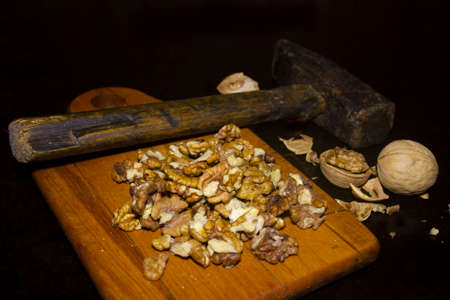 Kernels of chopped walnuts with an old hammer on a cutting board and whole nuts with shells ???????...