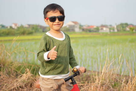 A handsome boy with sunglasses is playing a bicycle and shows his thumbs upの写真素材