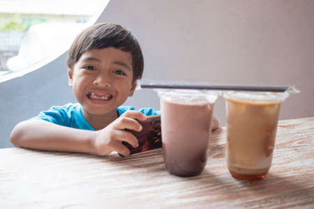 smiling handsome boy sitting and playing smartphone in cafeの写真素材