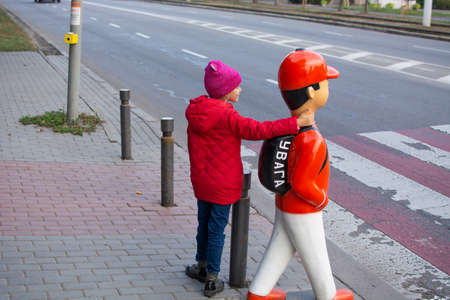 Little girl crosses the road at a pedestrian crossing. Sign warning kids on the road. Warning pedestrian sign near the childrens school.の写真素材