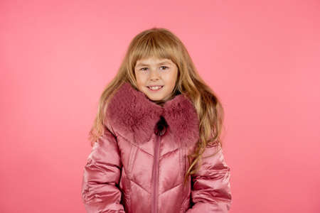Little girl in a winter pink coat on a pink background. Little fashionista trying on a pink coat.