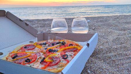 Closeup of box with delicious pizza with chease and salami with wineglass over view on ocean and sunsetの写真素材