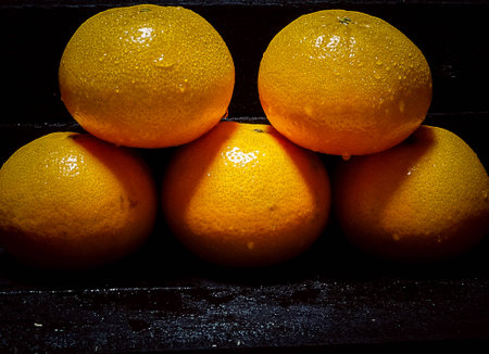 Close up the fresh oranges with water drops stacked on black timber wooden board,fresh fruit and fresh color,in abstract art design,contrast color between background and orange,art style,blurry light around.の写真素材