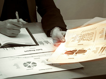 The business worker is taking of paper work from wooden desk,at office hour,investment chart and office work,blurry light background,vintage tone,art design.の写真素材