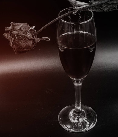 The abstract art design of a glass of red wine  and dried rose on black background,glamoru glow tone,art style,blurry light around.の写真素材