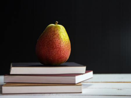 Closeup Pear put on three books stacked on wooden timber board,vintage warm light tone,blurry ligth design background.の写真素材