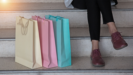 The pastel color of shopping bags put at the left side beside lady is sitting on the stairs ,after shopping at mall,vintage warm light tone.の写真素材