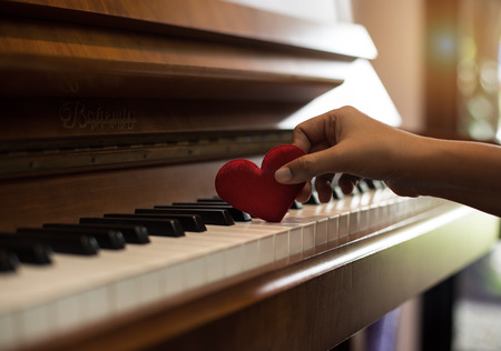 The small red heart was put on piano keys by human hand,warm light tone,reflection of sunlight is shining to piaone,beautiful background,blurry light aroundの写真素材