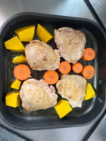 Cooking chicken thighs in a frying pan with fresh carrots and pumpkinの写真素材