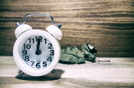 The abstract art design background of white alarm clock put on wooden timber board,in vintage and art tone,grainy old film style.の写真素材