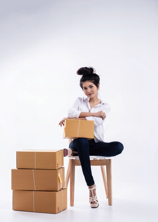The lady in white shirt and blue jean with shopping post box is posing by sitting with legs crossed on wooden chair,with smile and happy face,の写真素材