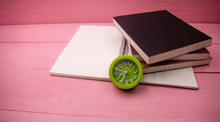 The green alarm clock put beside book stack,on pink wooden timber boardの写真素材