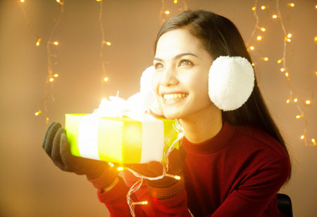 The beauty lady is wearing sweater,put earing to cover her ear,hold green gift box in hand,with...