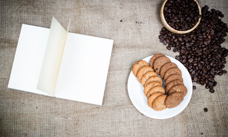 The opened book put beside dish of cookies and roasted coffee beans,on hemp clothの写真素材