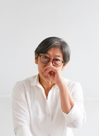 Old smart lady raise hand touch her nose,sign of she is not confident in yourself,with sad and depress feelingの写真素材