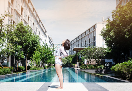The beauty lady is standing beside swimming pool,put her hand touch hip and turn face up in the...