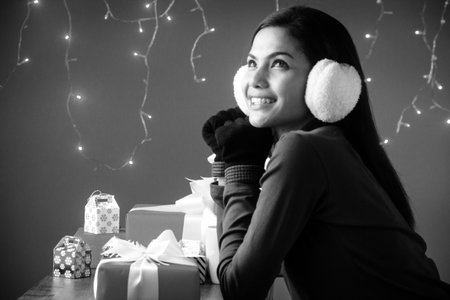 The beauty lady is wearing sweater,put earing to cover her ear,wear black glove,plenty of gift box on desk,black and white tone,blurry light around.の写真素材