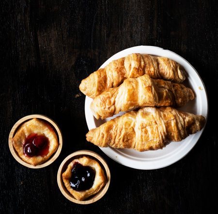 The croissant dish put beside blueberry pie in wooden cup,on wooden desk,vintage tone,blurry light aroundの写真素材
