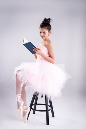 Beauty lady is wearing pink ballet dress and pink satin ballet shoes,sitting on black chair and read book,の写真素材