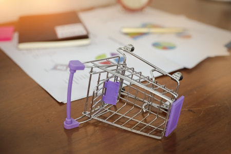 The shopping cart is lie on one side,on wooden desk,warm light tone,blurry light design backgroundの写真素材