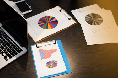 The business paper chart put beside laptop,on wooden desk,at office,warm light tone,blurry light aroundの写真素材