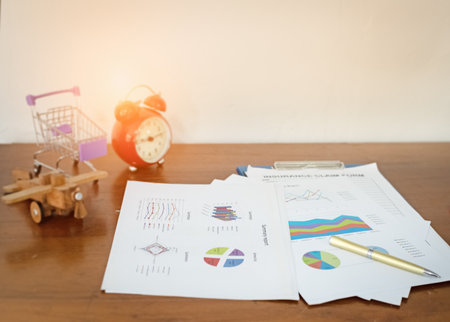 The business paper chart and pen put on wooden desk,warm light tone,blurry lightaroundの写真素材