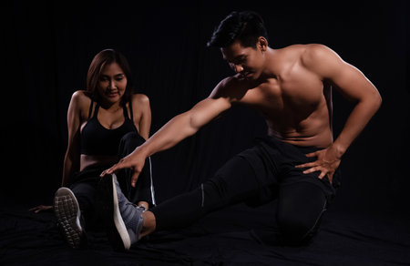 The man and woman are stretching on ground floor, with muscular torso on black background,show fit and firm body,strong muscleの写真素材