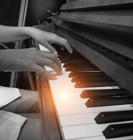 The human hand is pressing on piano key,playing music,black and white tone,blury light aroundの写真素材